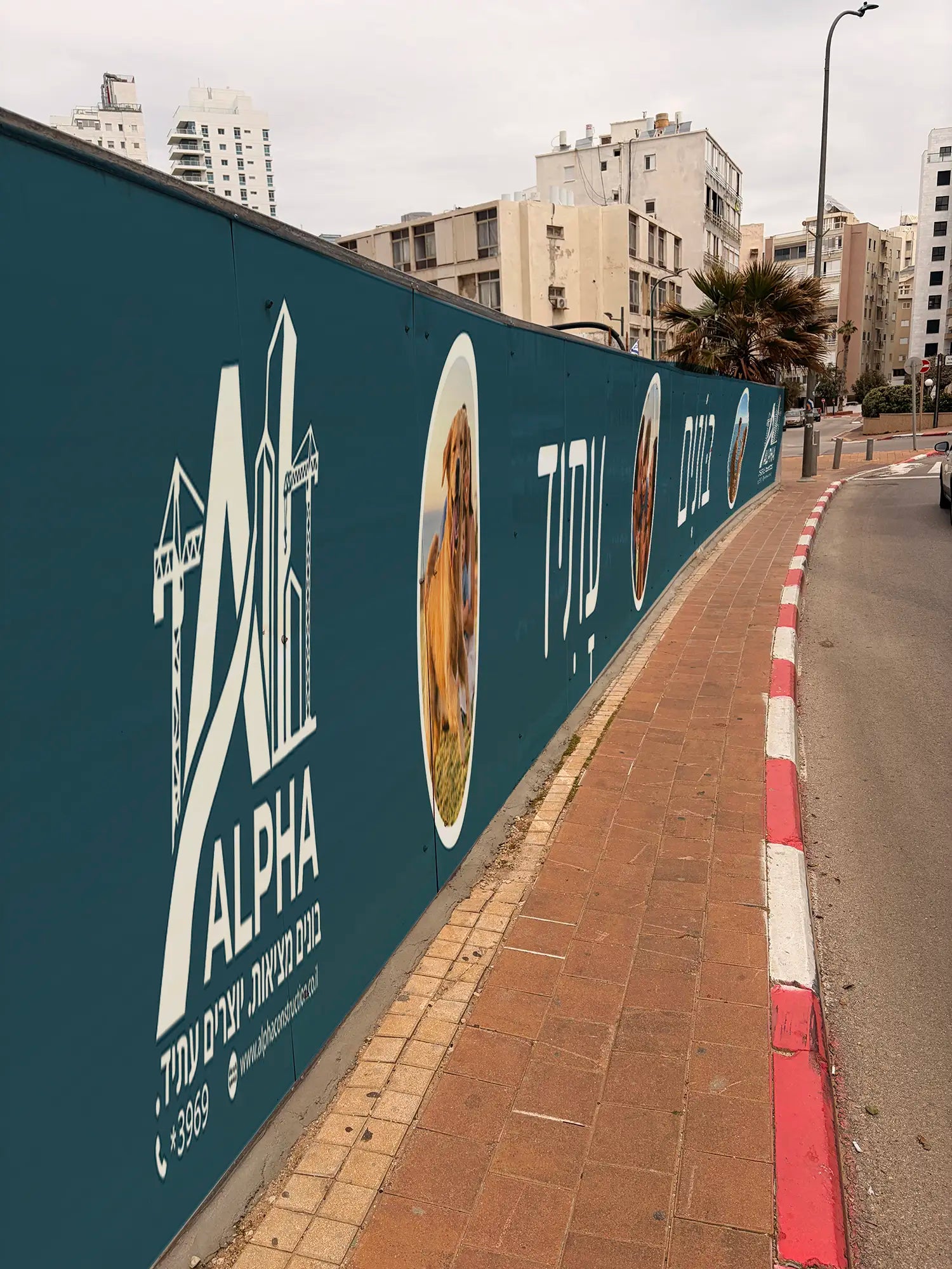 תקריב צדדי על גדר איסכורית ממותגת באתר בנייה, המציג שילוב של טקסט שיווקי ואייקוני בטיחות חובה המודפסים על מדבקת ויניל עמידה